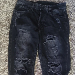 Svarta skinny jeans med slitningar - Säljer ett par svarta skinny jeans med coola slitningar. De är i denim och har en snygg, sliten look. Perfekta för en avslappnad och trendig stil. Till