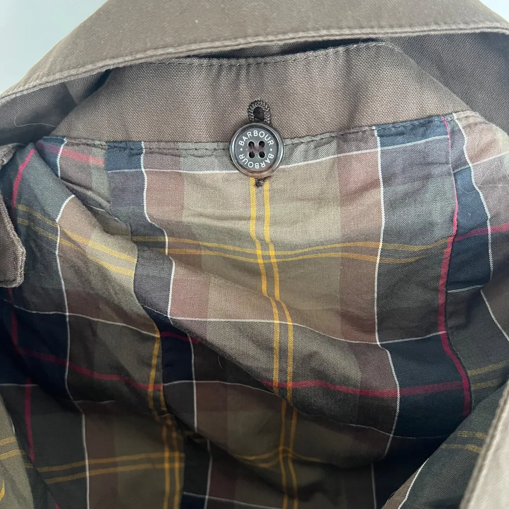 Säljer en snygg brun jacka från Barbour. Den är vattentät och andas, perfekt för höst och vår. Jackan har en klassisk design med knappar och en avtagbar huva. Insidan har ett stilrent rutigt mönster, jackan är lätt figur sydd. Den är i storlek 40 och passar perfekt för en stilren look. Oanvänd . Jackor.