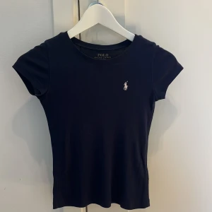 Marinblå t-shirt Ralph Lauren - Marinblå t-shirt Ralph Lauren  Storlek: 7 år (S) obs. Barnstorlek Fint skick, ej urtvättad. Dock en liten tråd som är lös vid halsen.  Djur och rökfritt hem.