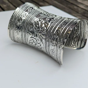 Brett silverfärgat armband/cuff armband med detaljerat mönster - Säljer ett supercoolt brett armband i silverfärg. Det har ett sjukt detaljerat och snyggt mönster med massor av snirkliga detaljer. Perfekt för att ge lite extra bling till din outfit!