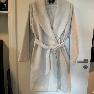 Kappa - Cremefärgad/gråvit kappa från Bikbok i storlek M. Diskreta fickor på sidan. I fint skick! 