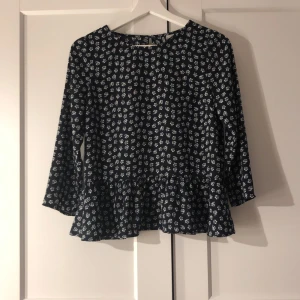 Blommig topp från H&M Divided - Säljer en söt blommig topp från H&M Divided i storlek XS. Den är svart med vita blommor och har en volangdetalj längst ner.och är perfekt för både vardag och fest. Superfin att matcha med jeans eller kjol!😘😘😘😘😘