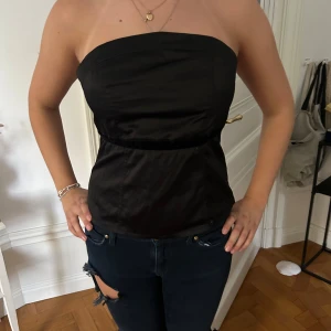 Svart topp  - Svart bandeau topp/ korsett i silkesliknande material med ett sidenband i midjan. Smock i ryggen vilket gör storleken flexibel. Det går att sätta in egna band. 