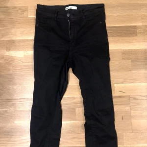 Svarta jeansbyxor - Säljer ett par svarta jeansbyxor i bra skick. De har en klassisk design med dragkedja och knappar framtill. Perfekta för både vardag och fest!