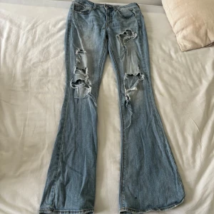 Bootcut jeans med hål - Jätte coola ljusblå jeans med hål från American eagle, passar mig i längden som är 171cm. Liten fläck längst ner vid högra benet vet inte om den går att få bort eller inte. Använd gärna köp nu❤️Strl 2 american eagle  