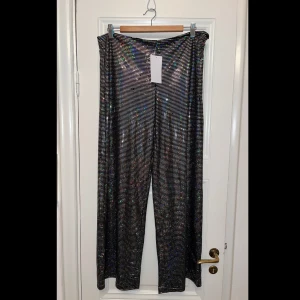 Glitter byxor! - Ascoola glitter / disco byxor från NA-KD! Helt oanvända med lappen kvar. Tänkte att jag skulle sy in dem men blev aldrig av. Storlek XL. Ny pris 300kr. De svarta plupparna är också ”paljett” och en del av designen. Dragkedja på höften.