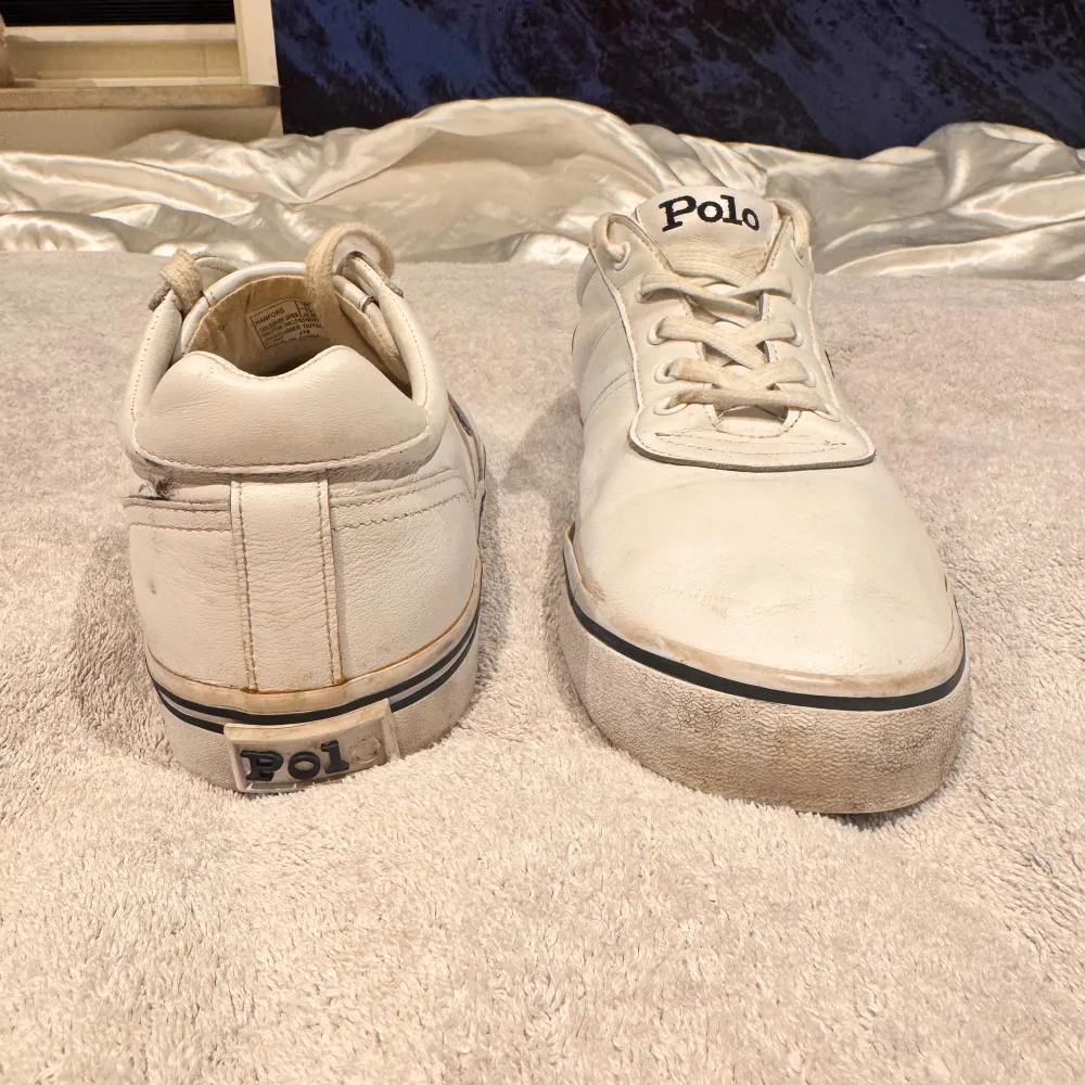 Säljer ett par vita sneakers från Polo Ralph Lauren. Skorna har en klassisk design med snörning och den ikoniska Polo-loggan på sidan. De är tillverkade i skinn med en gummisula, vilket gör dem både stiliga och bekväma. Perfekta för vardagsbruk!. Skor.