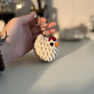 Virkad nyckelring med hönsdesign - Supergullig virkad nyckelring formad som en höna! Den är vit med en röd kam och orange näbb. Perfekt för att ge lite personlighet till dina nycklar eller väskan. Handgjord och unik, en rolig accessoar för alla djurälskare.