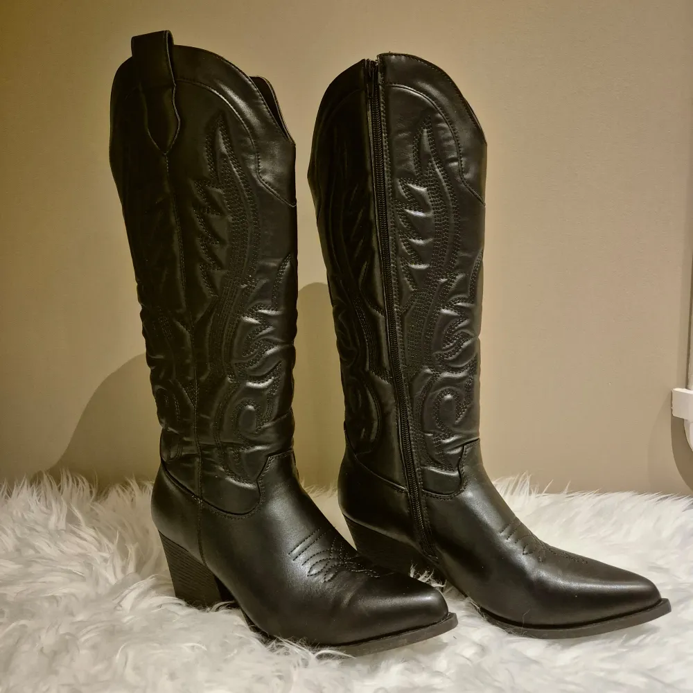 Svarta cowboyboots med broderade detaljer. Skorna är använda vid två tillfällen och är i perfekt skick utan skador. Höga som slutar strax under knät på mig som är 163. Storlek 39, men passar 38/39. Från New Yorker.. Kengät.