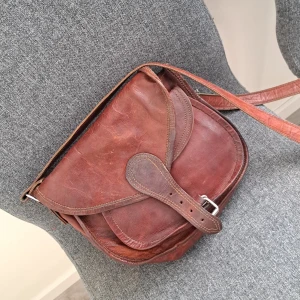 Brun axelväska i skinn från Gusti Leder - Säljer en snygg brun axelväska i skinn från Gusti Leder. Väskan har en klassisk design med ett spänne framtill och en justerbar axelrem. Perfekt för både vardag och speciella tillfällen!