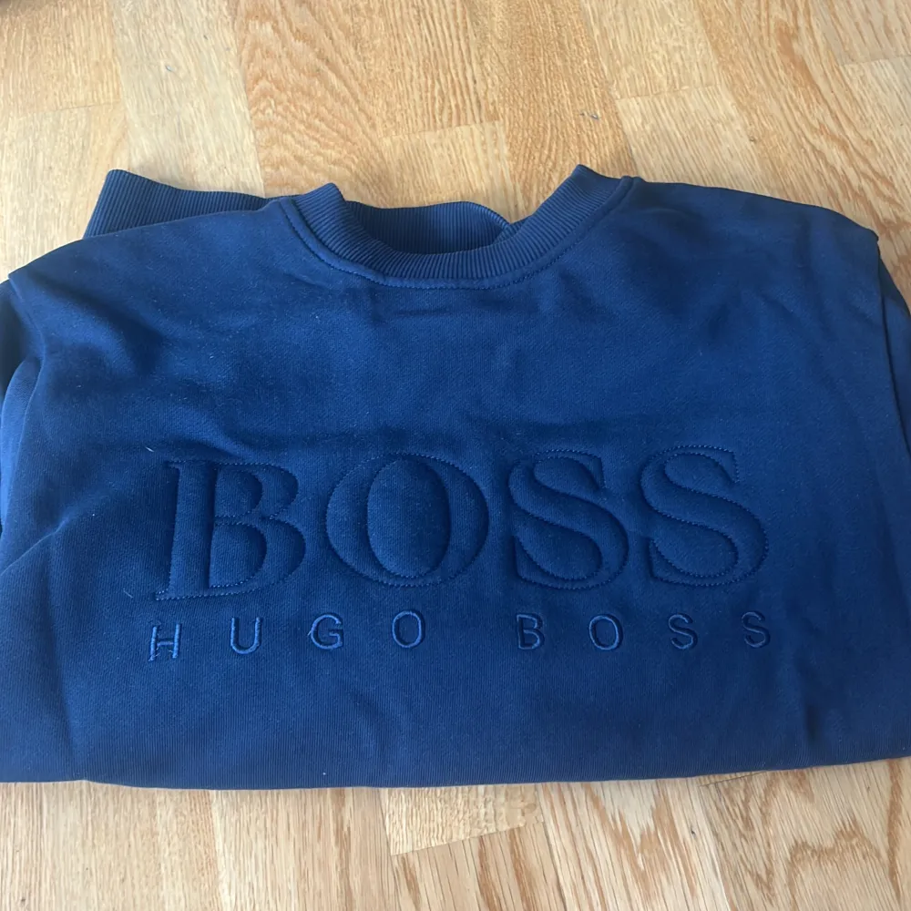 Säljer en snygg mörkblå tröja från Hugo Boss. Den har en broderad logga på framsidan som ger en stilren look. Tröjan är långärmad och gjord i ett mjukt material som känns skönt mot huden. Perfekt för både vardag och fest! använd fåtal gånger . Tröjor & Koftor.