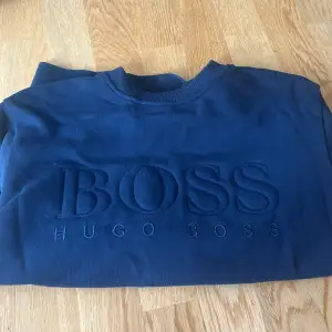 Säljer en snygg mörkblå tröja från Hugo Boss. Den har en broderad logga på framsidan som ger en stilren look. Tröjan är långärmad och gjord i ett mjukt material som känns skönt mot huden. Perfekt för både vardag och fest! använd fåtal gånger 