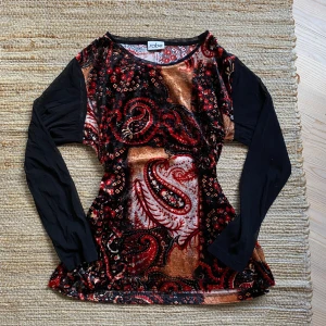 Mönstrad tröja från Rabe - Säljer en unik och färgglad tröja från Rabe. Den har ett coolt paisleymönster i rött, svart och brunt med inslag av blommor. Tröjan är långärmad med svarta ärmar och har en normal passform. Perfekt för höst och vinter!