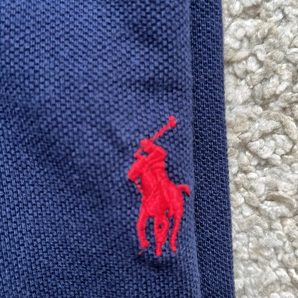 Säljer en klassisk mörkblå pikétröja från Polo Ralph Lauren. Den har en stilren design med två knappar och den ikoniska röda broderade loggan på bröstet. Perfekt för både vardag och lite finare tillfällen. Tröjan är i bra skick och redo för en ny ägare!. Tröjor & Koftor.