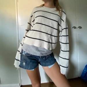 Vit och svart randig stickad tröja - Säljer en superfin vit stickad tröja med svarta ränder. Den är croppad och har en avslappnad passform som är perfekt för både vår och höst. Tröjan har långa ärmar och är riktigt mysig att ha på sig. Perfekt för en casual look med jeans eller shorts!
