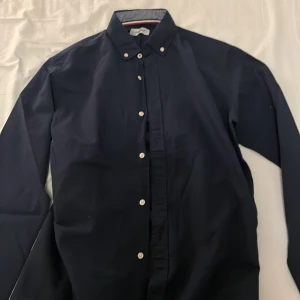 Mörkblå skjorta från Jack & Jones - Säljer en snygg mörkblå skjorta från Jack & Jones. Skjortan har långa ärmar och knappar längs hela framsidan. Perfekt för både vardag och fest. Den är i bra skick och gjord av bomull vilket gör den bekväm att bära. Passar perfekt till höst och vår!