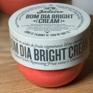 Sol de Janeiro  Bom Dia Bright Body Cream 75 ml - Säljer en härlig Bom Dia Bright Cream från Sol de Janeiro. Denna kroppskräm är berikad med fruktsyror och vitamin C för att ge huden en jämnare och ljusare ton. Den har en underbar doft av Cheirosa 40 och kommer i en snygg, korallfärgad burk. Perfekt
