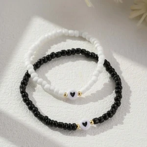 Svart och vitt pärlarmband med hjärtdetalj - Säljer ett set med två armband, ett svart och ett vitt, båda med små pärlor och en söt hjärtdetalj i mitten. Det svarta armbandet är 19 cm långt och det vita är 16 cm. Perfekt för par eller bästa vänner! 💖 Armbanden är hand gjorda så ni har den unika möjligheten att anpassa dem själva. Stötta en ung entreprenör med stora drömmar 
