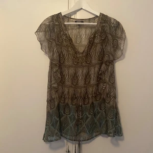 Mönstrad topp med knytning - Något använd, men bra skick Bronsdetaljer och knytning i midjan, fin både knyten och oknyten beroende på vilken passform man vill ha. 