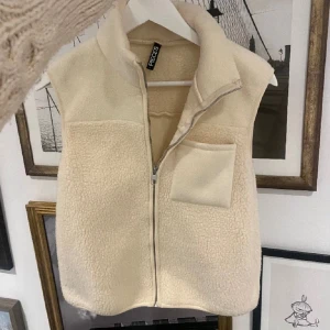 Beige teddyväst från Pieces - Säljer en supermysig beige teddyväst från Pieces i storlek XS. Västen har en dragkedja framtill och en praktisk bröstficka. Perfekt för höst och vinter när du vill hålla dig varm och snygg. Den är i nyskick och redo att användas direkt!