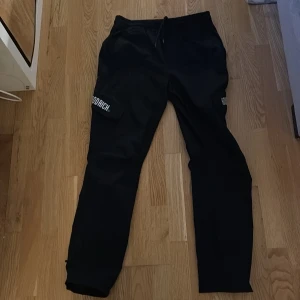 Svarta cargo-pants, Hoodrich  - Snygga svarta cargo byxor från Hoodrich med tryck på benen. Byxorna har en normal passform och är perfekta för en avslappnad stil. De har praktiska fickor och en elastisk midja för extra komfort. Byxorna är wide i benen och i ett mycket bra skick!