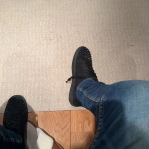 Christian louboutin - Snygga svarta sneakers från Christian Louboutin med nitar på tån och den ikoniska röda sulan. Skorna har snörning och är tillverkade i mocka, vilket ger en lyxig känsla.
