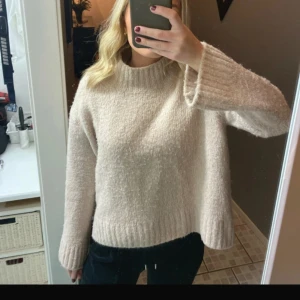 Beige stickad tröja - Mysig beige stickad tröja med långa ärmar och ribbade detaljer vid ärmslut och nederkant. Perfekt för kyliga dagar.