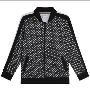 Svartvit mönstrad jacka från BOSS - Snygg svartvit mönstrad jacka från BOSS med dragkedja och ribbade muddar. Jackan har ett unikt rutigt mönster och svarta detaljer vid ärmar och krage. Perfekt för en stilren look.