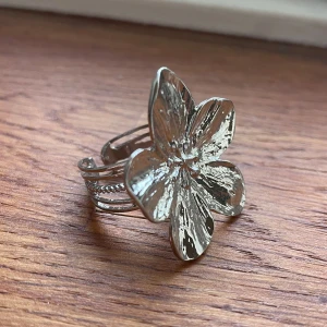 Silvrig blomring - Snygg ring i silver med en stor blomma som motiv. Fin design med flera band som ger en unik look. Perfekt för att ge en extra touch till din outfit! Helt ny!