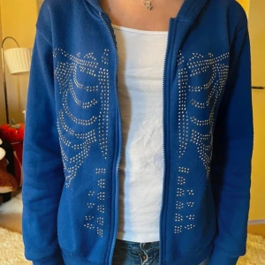 Blå huvtröja med skelett detaljer - Snygg blå huvtröja med dragkedja och coola nitdetaljer i form av skelettmönster på framsidan. Perfekt för en unik och edgy stil. Tröjan har långa ärmar och en bekväm passform💙!