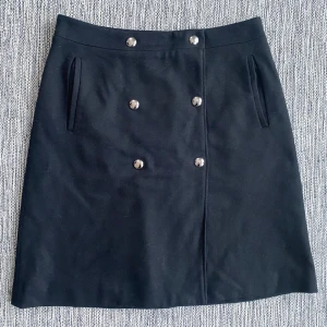 Ny svart omlottkjol i strl M från Filippa K i ull, modell wrap button skirt - Ny svart omlottkjol i strl M från Filippa K i ull, modell wrap button skirt.  Ny, aldrig använd   Mått Midjan: ca 40 cm Total längd: ca 55 cm  Kjol 80% ull och 20% polyamid Underkjol 54% viskos och 46% polyester   Kommer från ett djur och rökfritt hem.