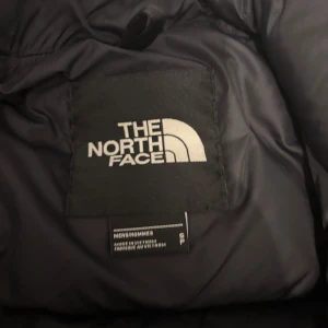 Svart dunjacka från The North Face - Säljer en svart pufferjacka från The North Face. Jackan har en hög krage och dragkedja framtill. Perfekt för kalla dagar samt håller värmen. Klassisk och stilren look som passar till det mesta. Sälj pga att den inte är direkt min stil och där av är den aldrig använd 