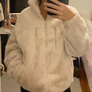 Beige teddyjacka med dragkedja - Mysig beige teddyjacka med dragkedja framtill. Jackan har en oversized passform och långa ärmar, perfekt för kyliga dagar. Den fluffiga texturen ger en trendig look.