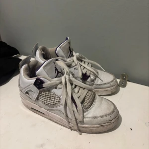 Vita Nike Air Jordans med lila detaljer - Säljer ett par vita Nike Air Jordans med lila detaljer. Skorna har snörning och en klassisk design med synlig luftdämpning i sulan. Perfekta för dig som älskar en sportig stil med en touch av färg.