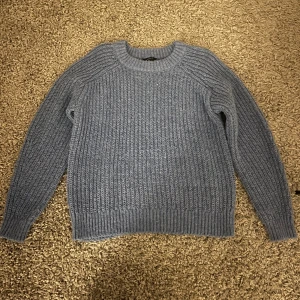 Blå stickad tröja - Mysig blå stickad tröja med rund hals och långa ärmar. Perfekt för kyliga dagar och ger en avslappnad stil. Ribbstickade detaljer vid ärmslut och nederkant.