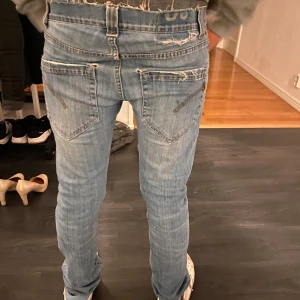  Dondup Ljusblå jeans med fransiga kanter - Säljer ett par ljusblå jeans med fransiga kanter och klassisk femficksdesign. Jeansen har en normal passform och är perfekta för en avslappnad stil. De är tillverkade i denim och har en snygg tvättad look.