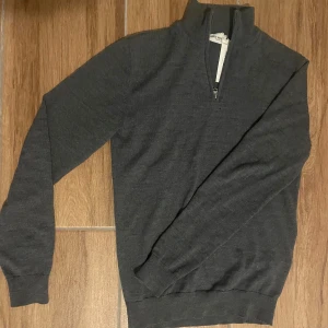 Mörkgrå zip-tröja från John Henric - Säljer en stilren mörkgrå tröja från John Henric med halv dragkedja. Perfekt för kyligare dagar med sin mjuka och bekväma passform. Tröjan har långa ärmar och ribbade muddar. Materialet är 100% merino ull. Ny pris 1200kr säljer för endast 599kr! Hör av er vid frågor och funderingar!