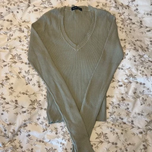 Olivgrön ribbad tröja från Brandy Melville - Säljer en stilren olivgrön ribbad tröja från Brandy Melville med v-ringning. Tröjan har långa ärmar och är perfekt för lager-på-lager under kyligare dagar. Passar både till jeans och kjol för en avslappnad look.