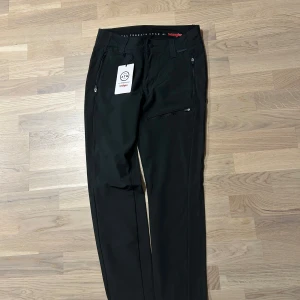 Svarta byxor från Wrangler - Snygga svarta byxor från Wrangler med dragkedjedetaljer. Perfekta för en stilren look. Byxorna har en normal passform och är tillverkade i ett slitstarkt material. Helt oanvända med prislappen kvar. Inköpspris 599kr.