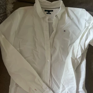 Vit skjorta från Tommy Hilfiger - Säljer en stilren vit skjorta från Tommy Hilfiger i slim fit. Skjortan har långa ärmar och klassiska knappar framtill. Perfekt för en elegant look.