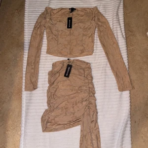 Beige tvådelad klänning - Trendig tvådelad klänning i beige med långärmad topp och matchande kjol. Setet har en stilren design med ett subtilt mönster och en smickrande passform. Perfekt för en chic look.