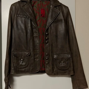 Brun skinnjacka med knappar - Vintage mörkbrun skinnjacka från Goldstein med knappar framtill och på ärmsluten. Den är knappt använd. 