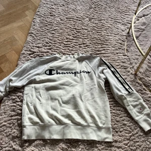 Vit sweatshirt från Champion - Säljer en vit sweatshirt från Champion med svart logga på bröstet och längs ärmarna. Så skönt material och i princip oanvänd. Går att köpa matchande byxor till också!💗
