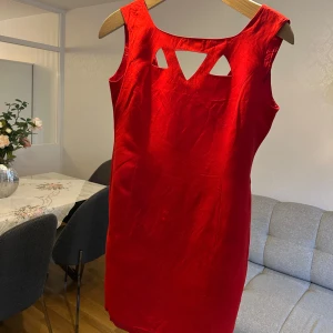 Röd klänning från Mondi - Snygg röd klänning från Mondi med djup v-ringning och unika detaljer på ryggen. Klänningen har en dragkedja bak och är ärmlös, vilket ger en elegant look. Perfekt för speciella tillfällen.