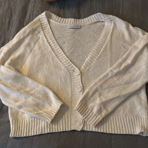 Vit kofta från Stradivarius - Mysig vit kofta från Stradivarius med v-ringning och knappar framtill. 