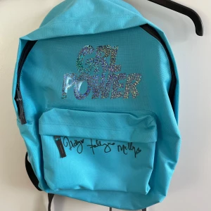 Blå ryggsäck med glittrig text från dolly style - Cool blå ryggsäck med texten 'Girl Power' i glittriga bokstäver. Den har en framficka med dragkedja och vadderade axelremmar för extra komfort. Från dolly styles kollektion med deras signaturer. Är från en konsert! Tillkommer ett riktig dolly style roset diadem, så man kan matcha med väskan. Aldrig använd, så passa på. Allt är äkta och är från en av deras konserter!!😍