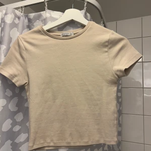 Beige t-shirt - Säljer en enkel och stilren beige t-shirt. Den har en rund halsringning och korta ärmar, perfekt för en avslappnad look.