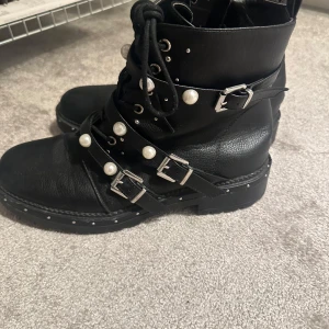 Svarta boots med pärldetaljer - Snygga svarta boots med snörning och dekorativa pärlor. Skorna har flera spännen och en dragkedja på sidan för enkel på- och avtagning.