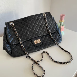 Svart quiltad axelväska - Snygg svart quiltad axelväska med kedjedetaljer och en praktisk dragkedja på baksidan. Perfekt för att ge en elegant touch till din outfit.