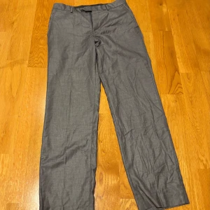 Grå kostymbyxor - Snygga grå kostymbyxor med rak passform. Perfekta för en stilren look. Byxorna har knappar bak och en klassisk design som passar till många tillfällen.